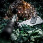 Skaidrus-juodas deklas Tactical Quantum Stealth telefonui Apple iPhone 15 ant zemes tarp zalumos