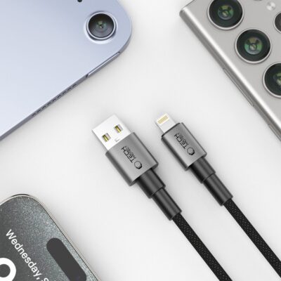 Pilkas kabelis TECH-PROTECT ULTRABOOST DNA LIGHTNING CABLE 15W/2.4A 100CM su USB ir Lightning jungtimis ant balto paviršiaus tarp mobiliųjų įrenginių