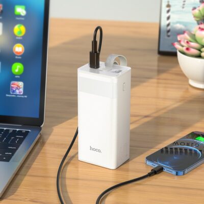 Balta išorinė baterija Power Bank Hoco J86 22.5W Quick Charge 3.0 40000mAh ant stalo prie nešiojamo kompiuterio ir telefono
